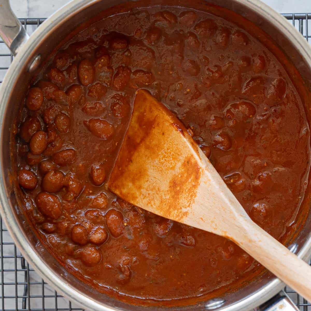 A saucepan of beans in a rich dark red glossy sauce.