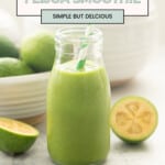 A small glass bottle of green smoothie with a green and white striped straw, a bowl of feijoas in the background. With text overlay for Pinterest: The best feijoa smoothie.