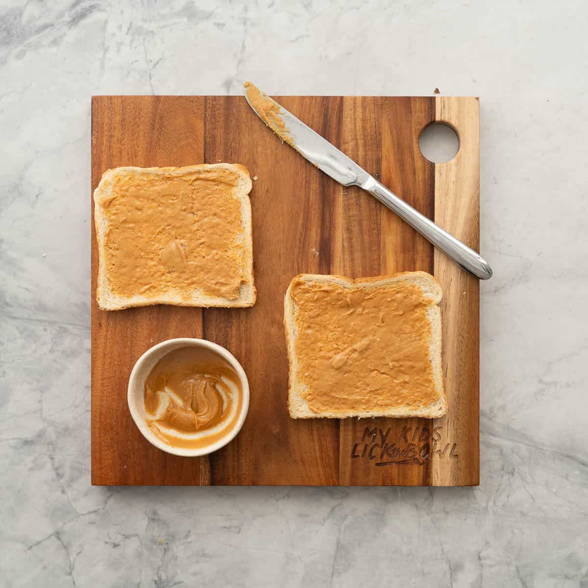 Two slices of bread, spread with peanut butter resting on a wooden chopping board.