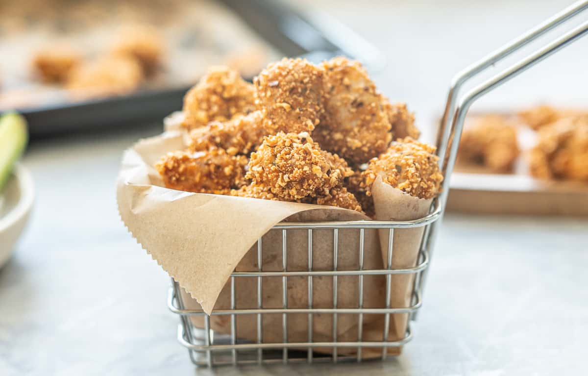 A small metal basket lined with brown parchment paper filled with popcorn chicken. 