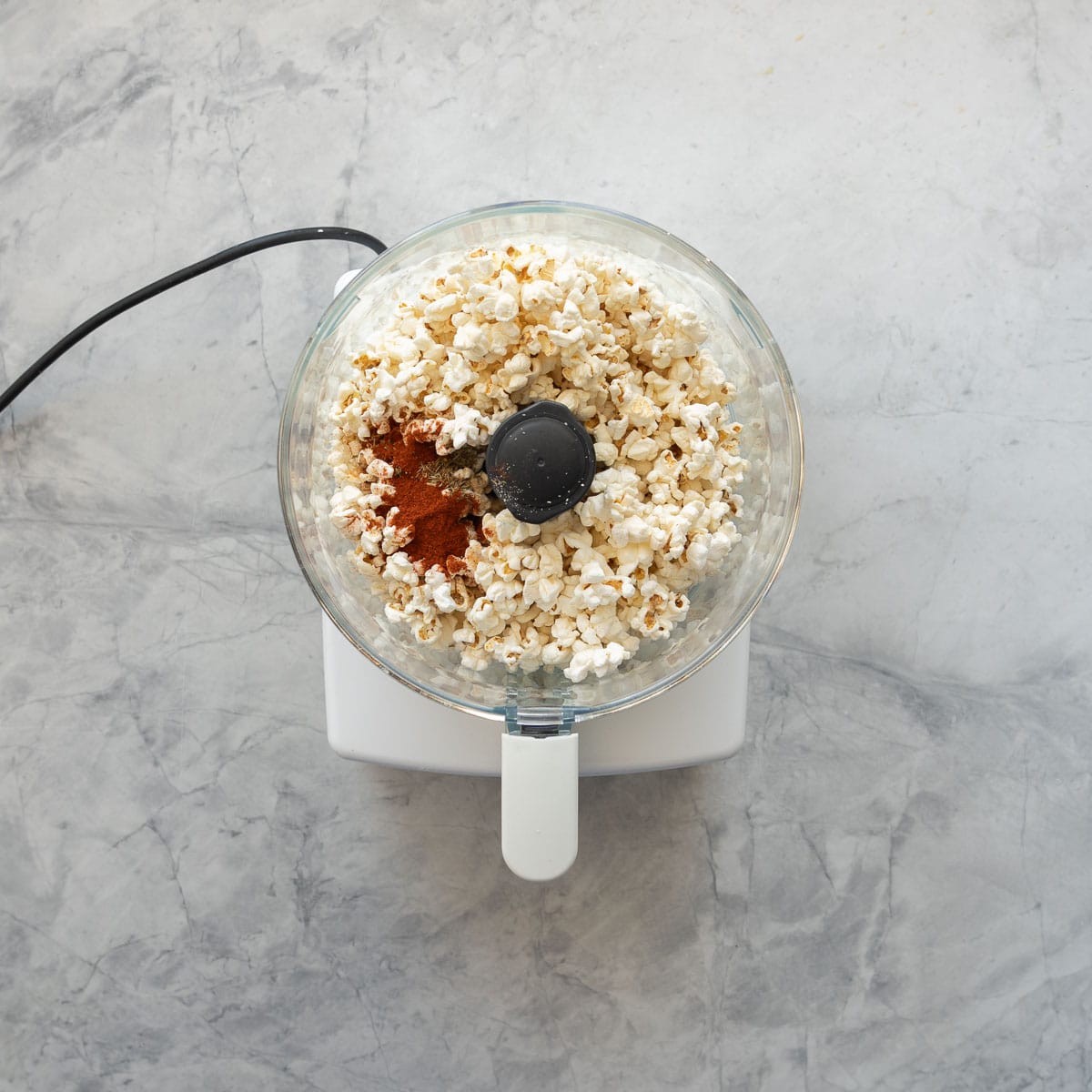 A food processor with popcorn and spices in the vessel. 