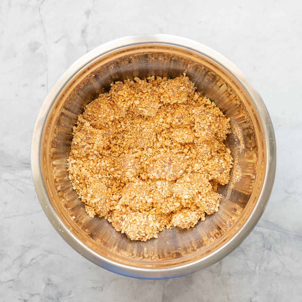 Cubed chicken coated in popcorn crumb in a stainless steel mixing bowl. 