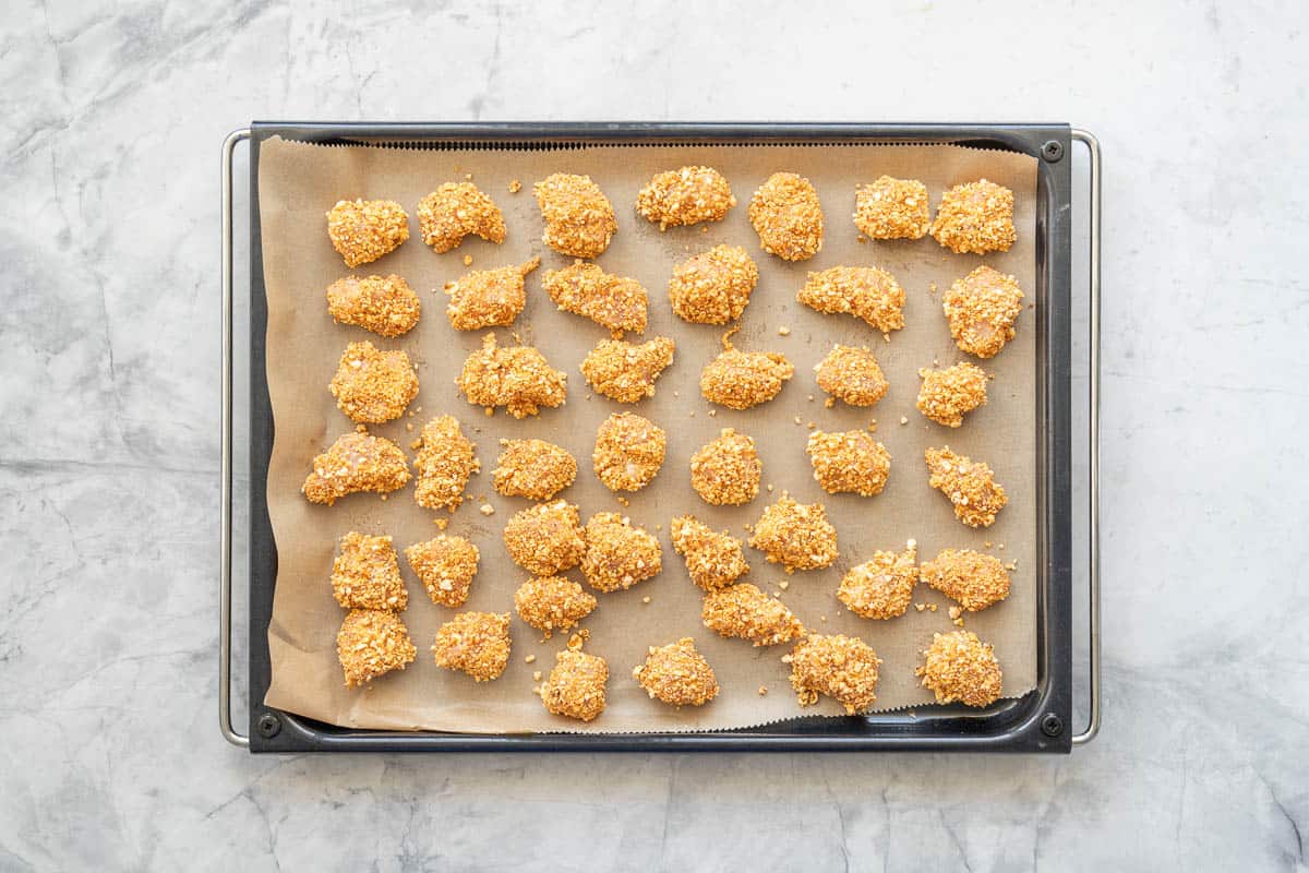 Popcorn crusted chicken on a lined baking tray. 