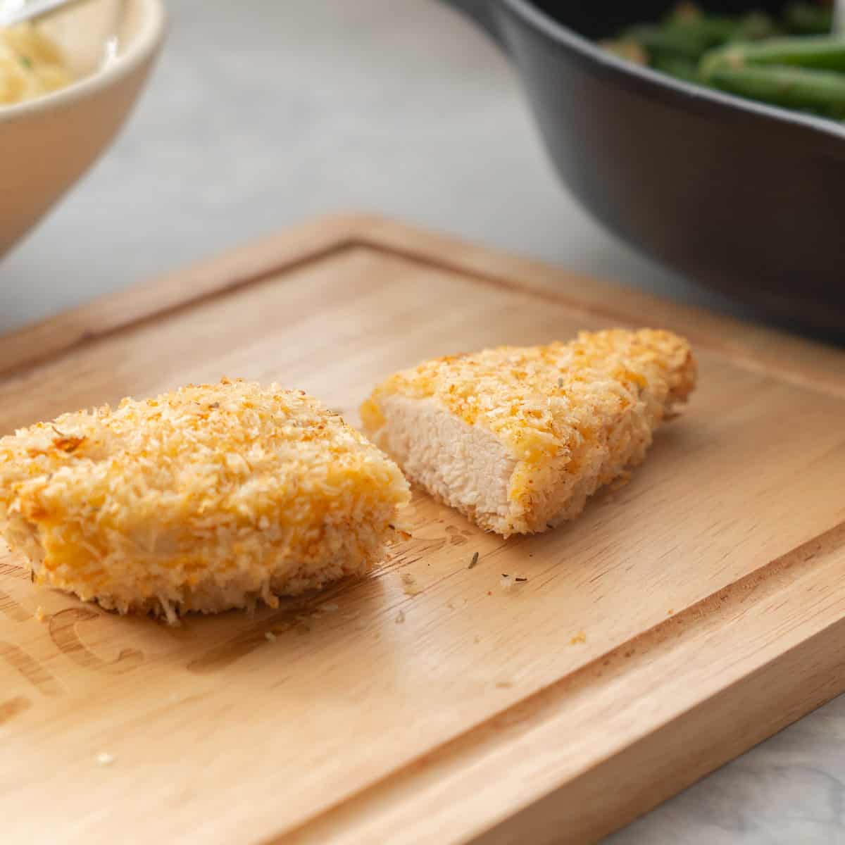 A crumbed piece of chicken cut in half on a wooden chopping board.