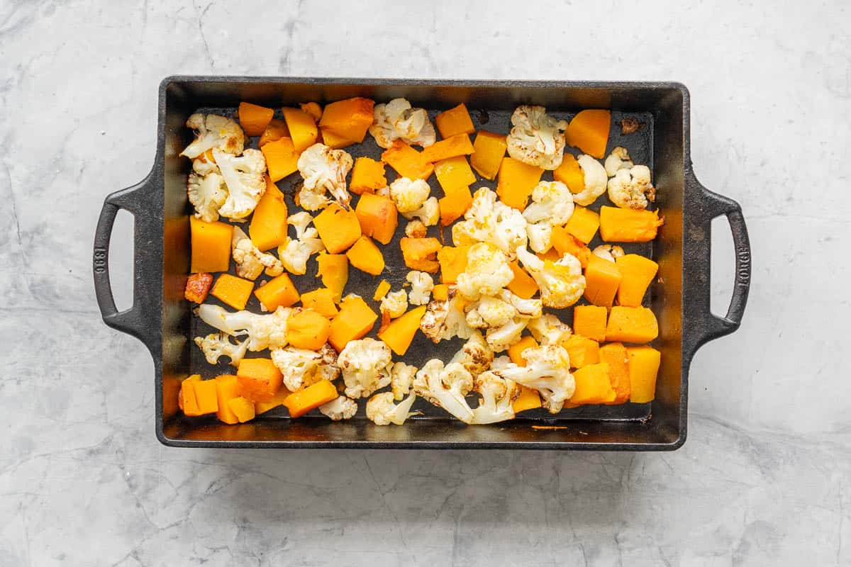 Roasted cauliflower florets and pieces of pumpkin in a cast iron roasting dish. 