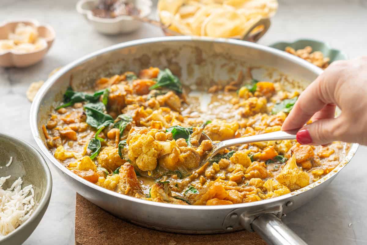Chickpea, pumpkin and cauliflower curry being served from a skillet with a large spoon. 