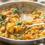 Chickpea, pumpkin and cauliflower curry being served from a skillet with a large spoon.