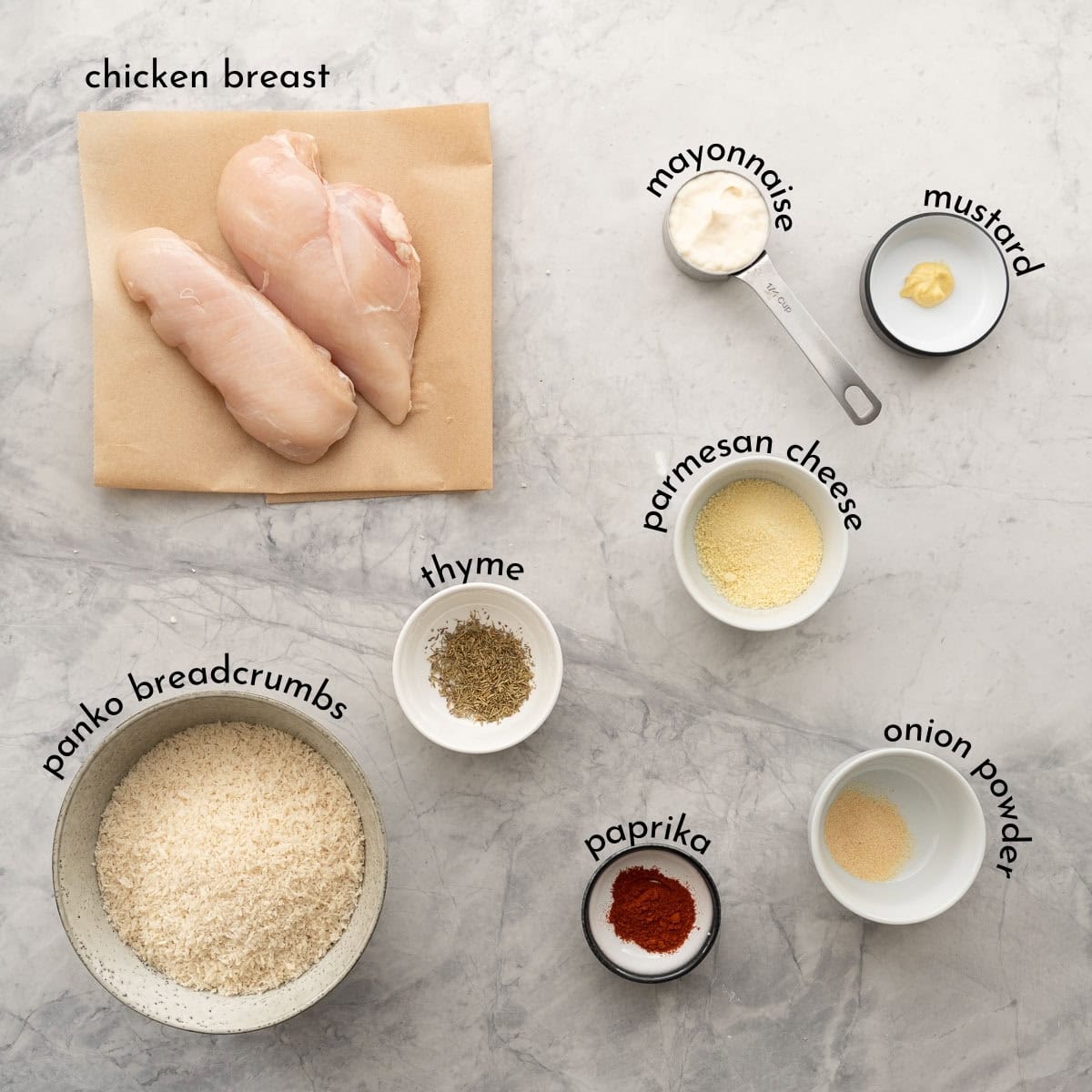 The ingredients to make baked chicken cutlets laid out on a bench top with text overlay labels. 