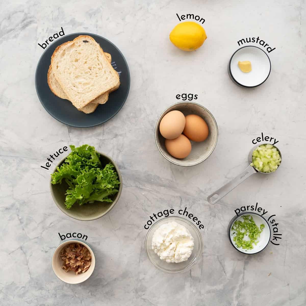 The ingredients to make egg salad laid out on a bench top in bowls with text overlay ingredient labels.