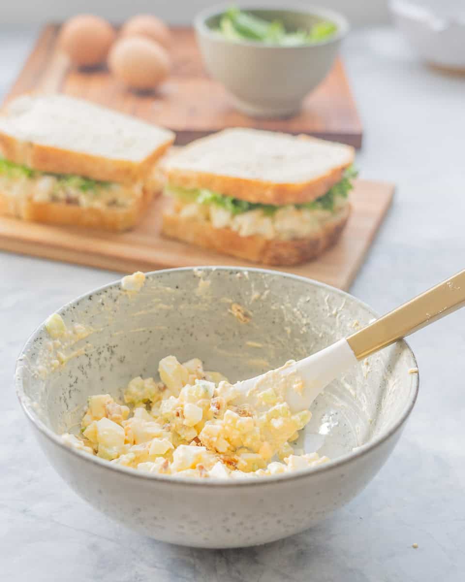 A bowl of egg salad and rubber spatula with a brass handle. 