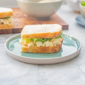 An egg salad sandwich on a turquoise plate with a second sandwich in the background.