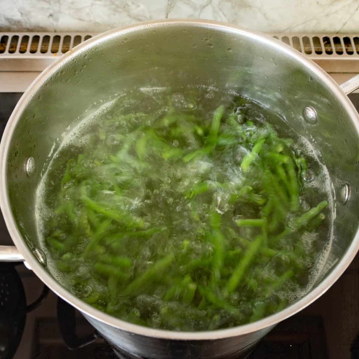 A large saucepan of rapid boiling water and green beans. 