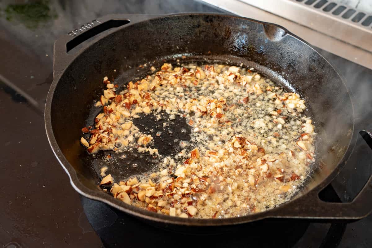 A cast iron skillet with chopped nuts sautéeing in butter and oil. 