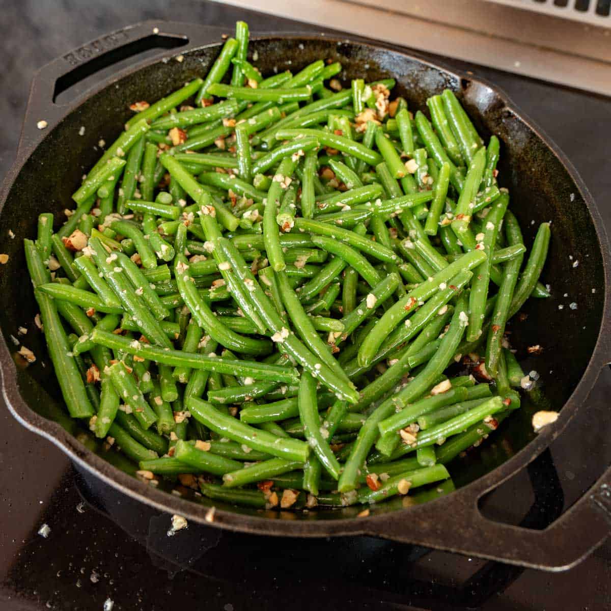A cast iron skillet of garlic butter coated green beans. 