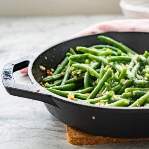 A cast iron skillet of green beans glistening with butter and small pieces of chopped almond.