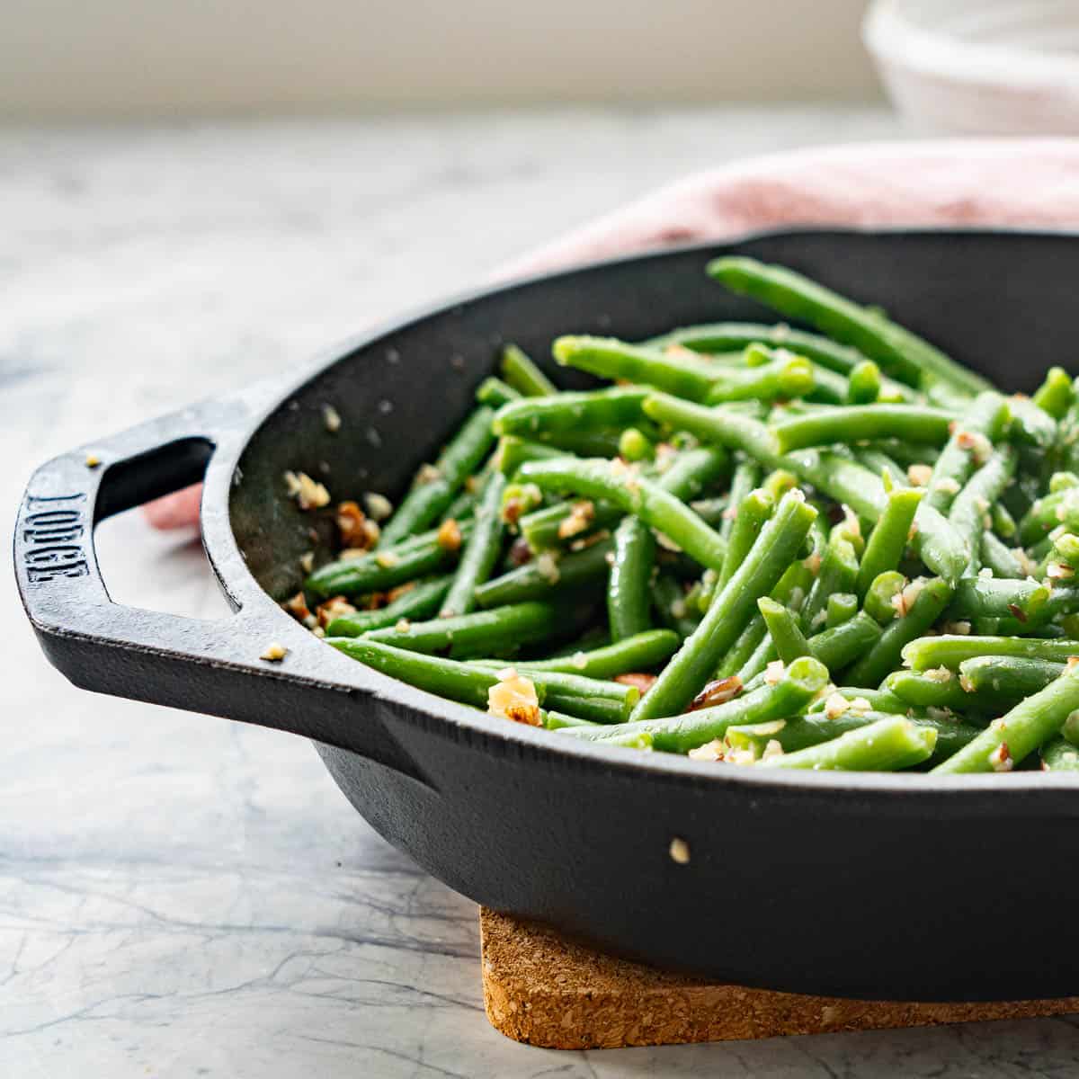 A lodge cast iron skillet filled with cooked green beans, small pieces of garlic and almond pieces visible on the beans. 
