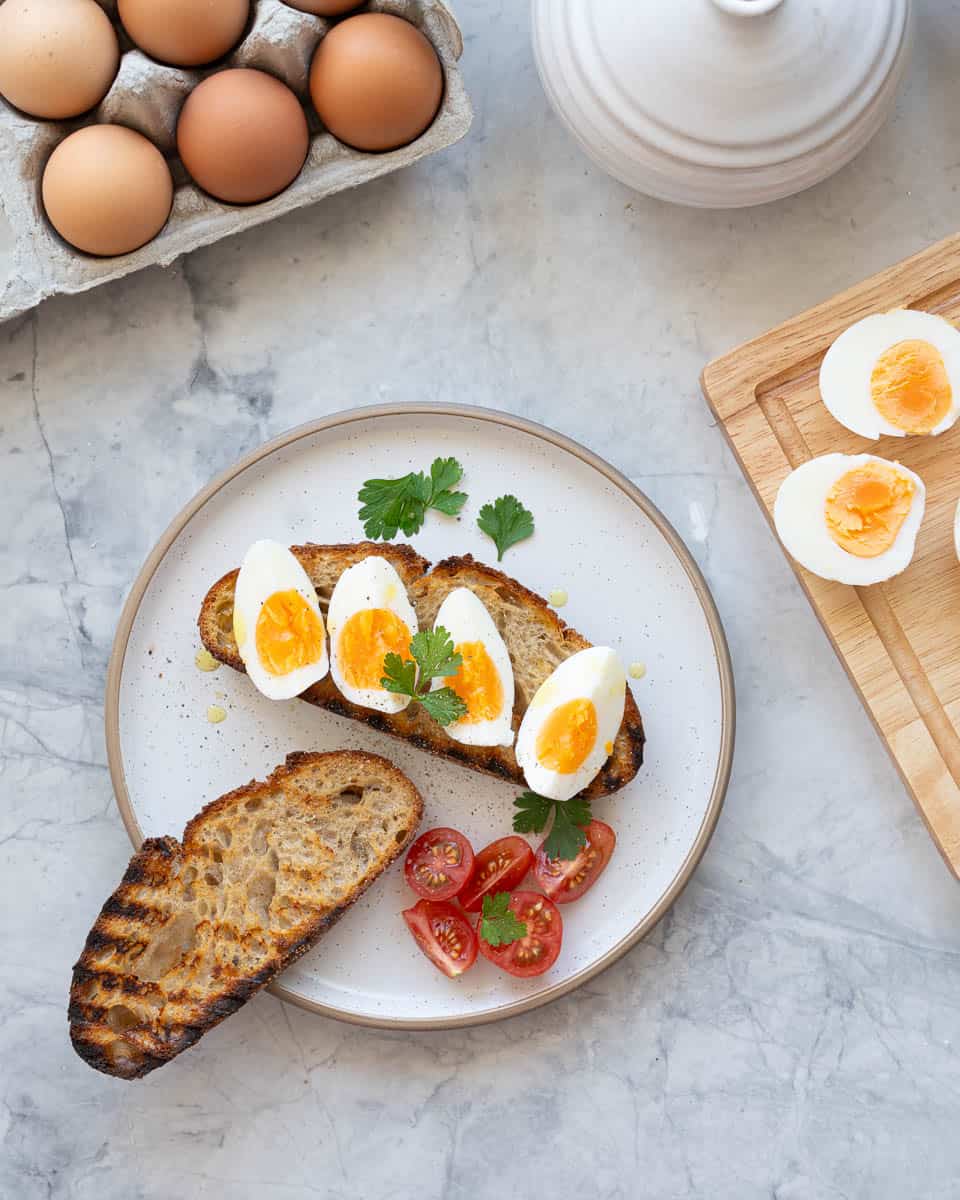 A side plate with two pieces of grilled toast, one topped with four pieces of hard boiled eggs and sprigs of parsley.