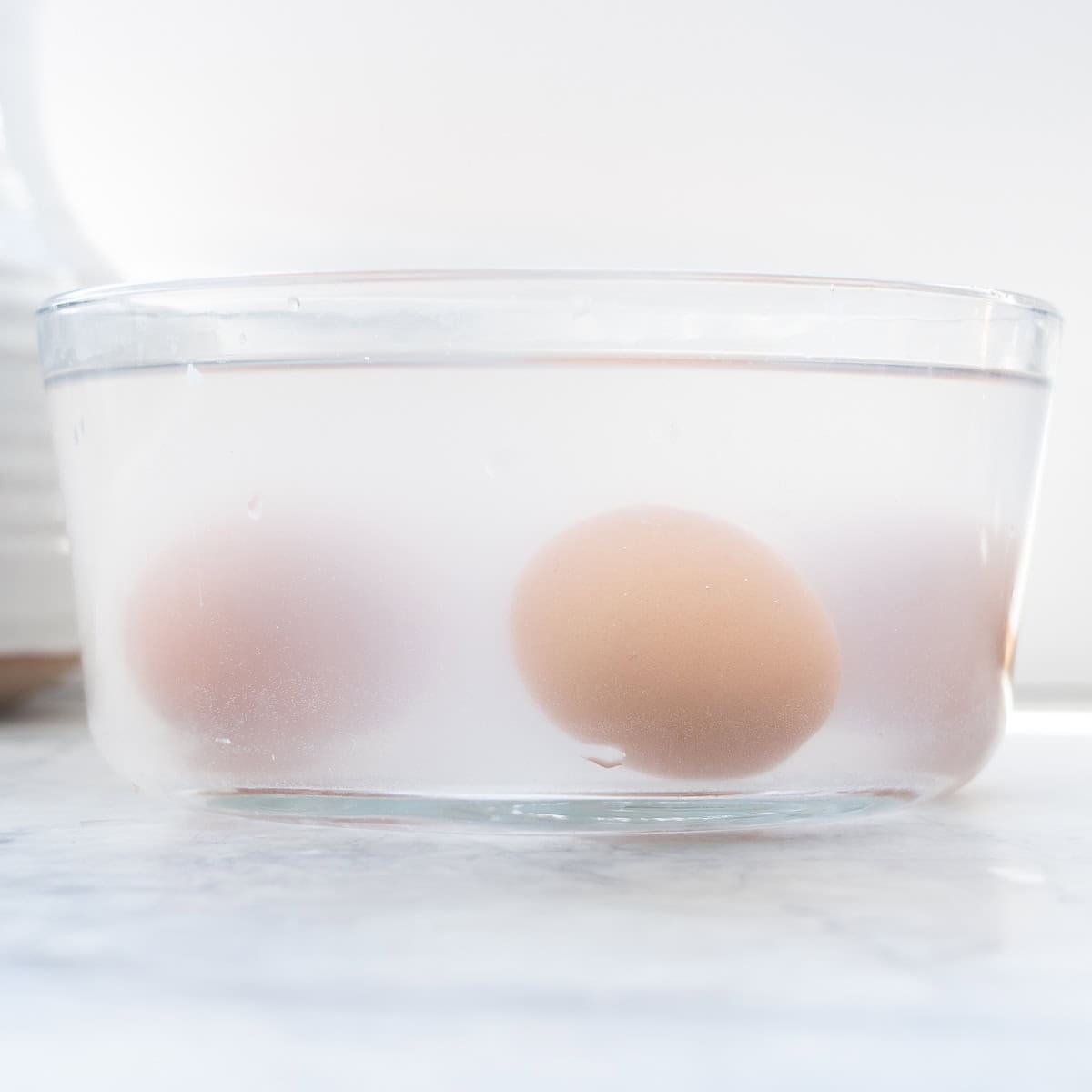 Three eggs visible in a microwave proof bowl filled with water.