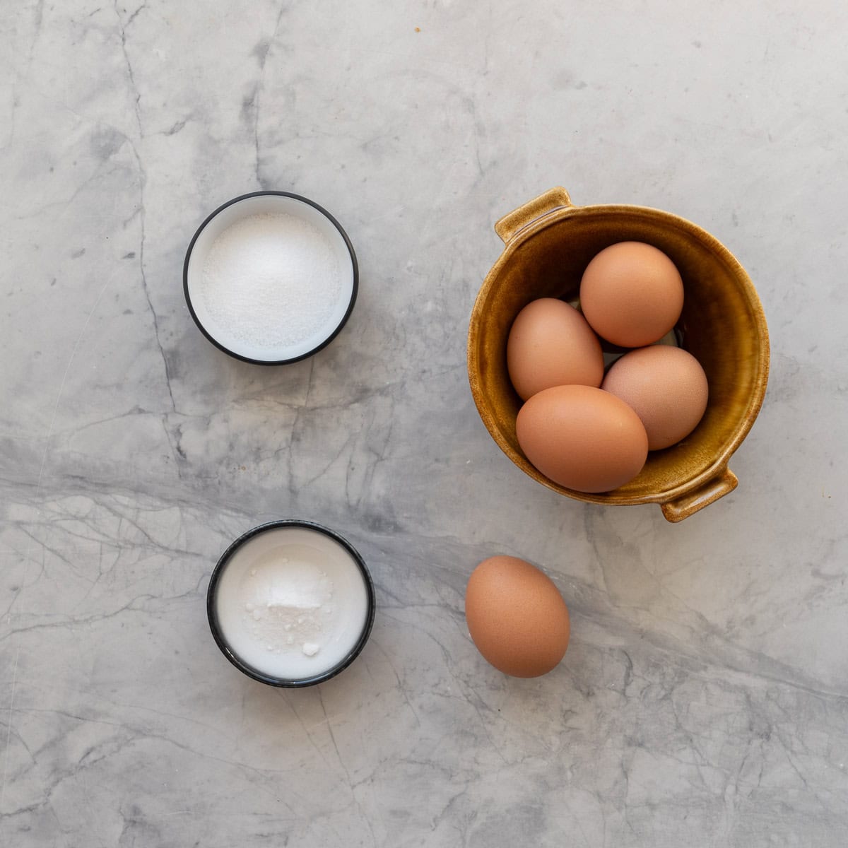 A ceramic bowl of egg, next to two ramekins holding white powders.