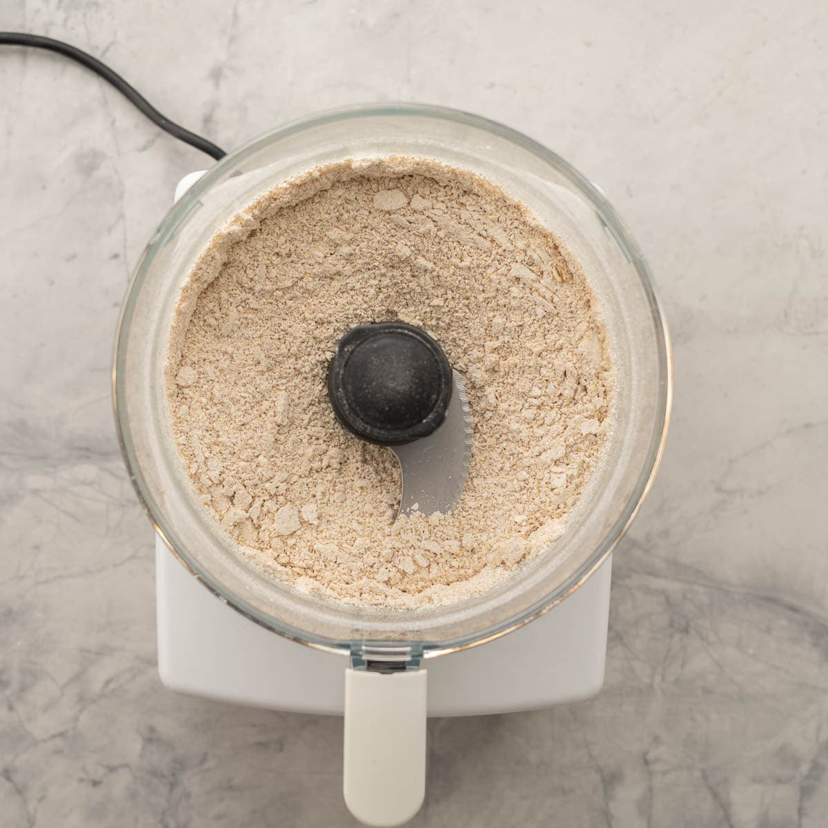 A food processor full of blitzed oats resting on the bench