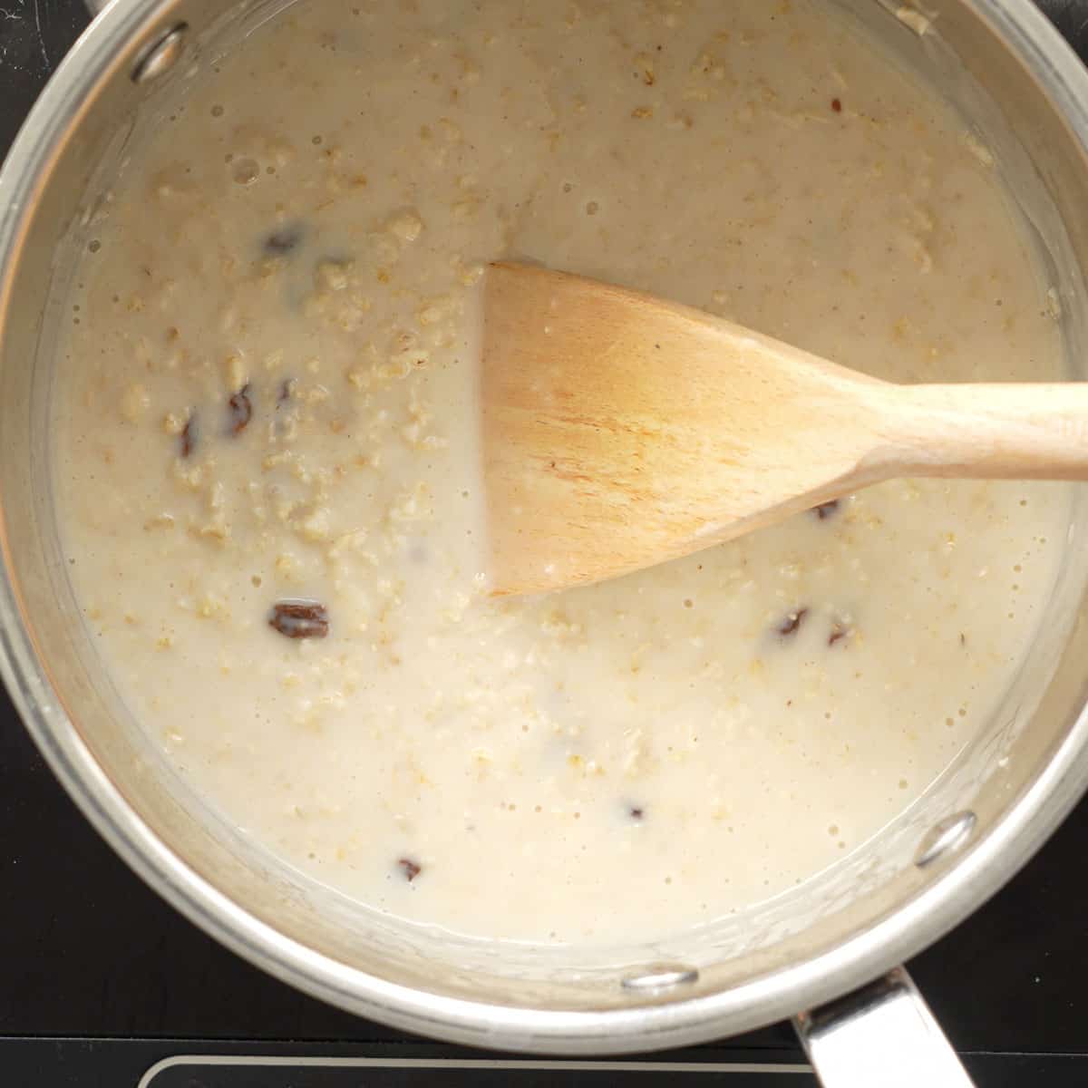A saucepan of very creamy oatmeal in a sauce pan with raisins visible.