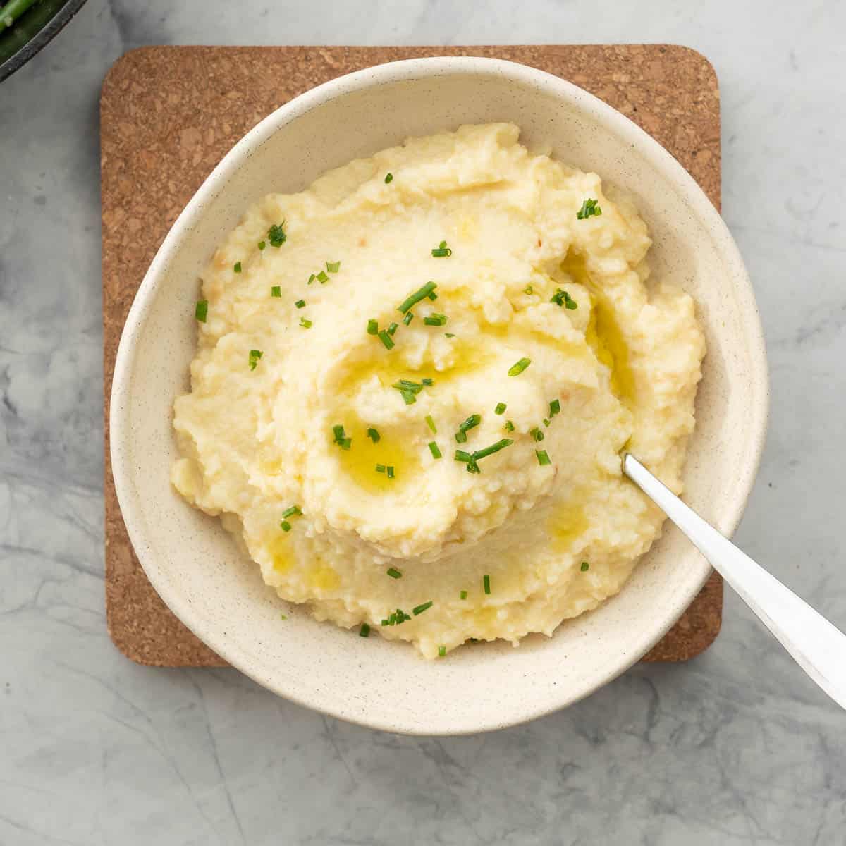 A bowl of potato and cauliflower mash, drizzled with olive oil and sprinkled with chopped chives. 