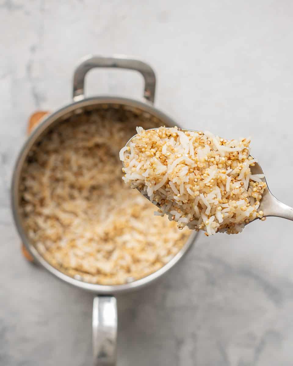 A large spoon of cooked quinoa and rice being scooped out of a saucepan. 