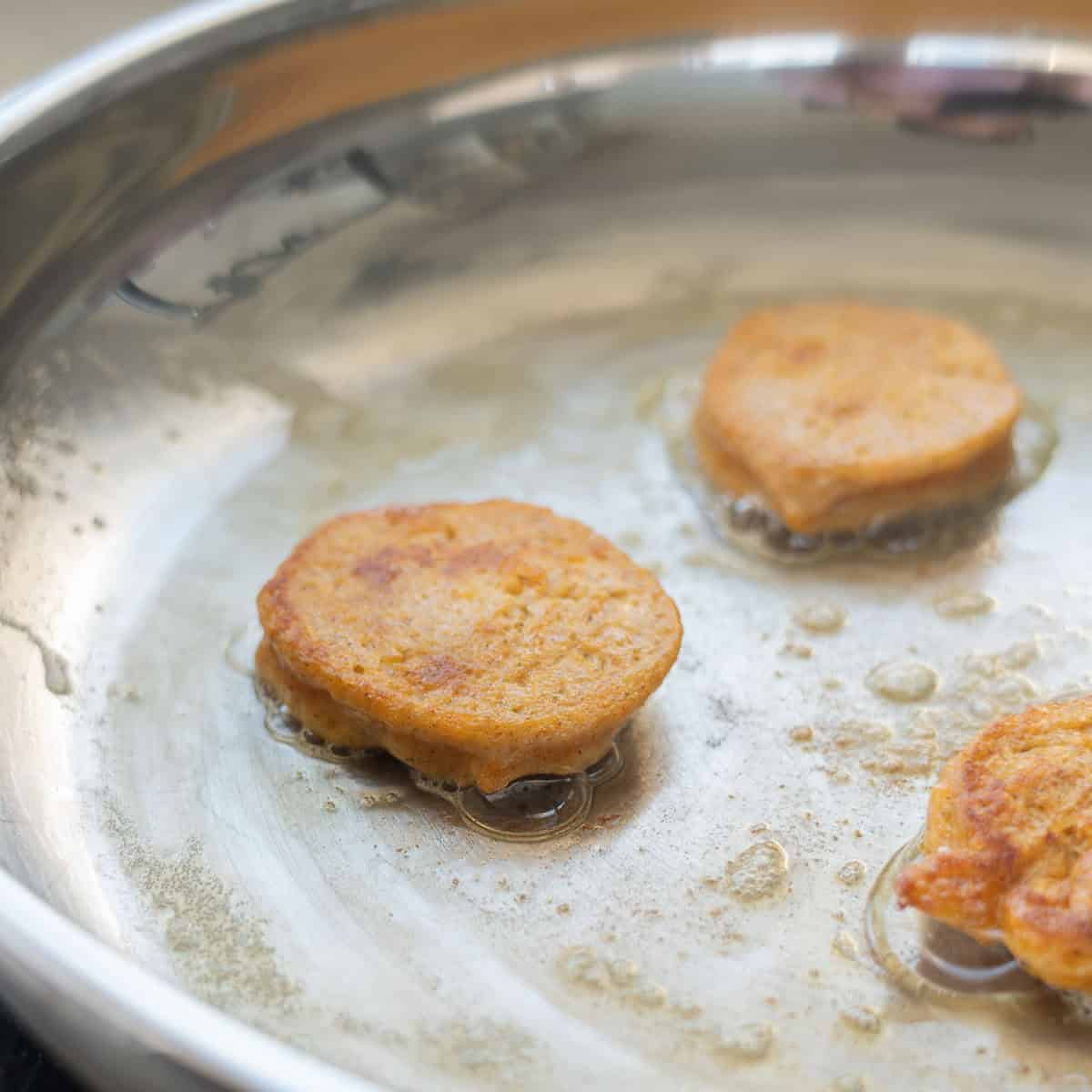 A close up of a golden brown pancakes cooking in butter on a skillet.