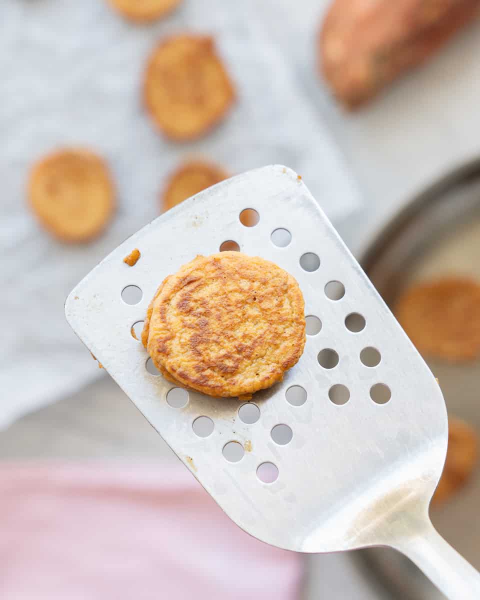 A small pancake being lifted up on a slotted stainless steel spatula. 