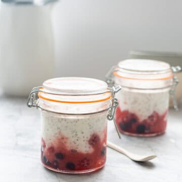 2 closed glass jars sitting filled with a layer of berries topped with chia yogurt on a bench top.