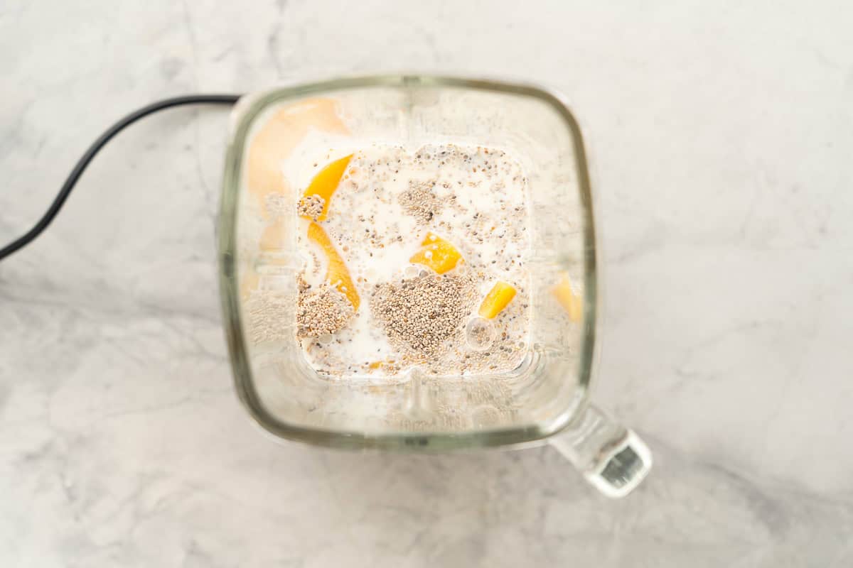 Looking down into a blender of milk, chia seeds and canned peaches. 