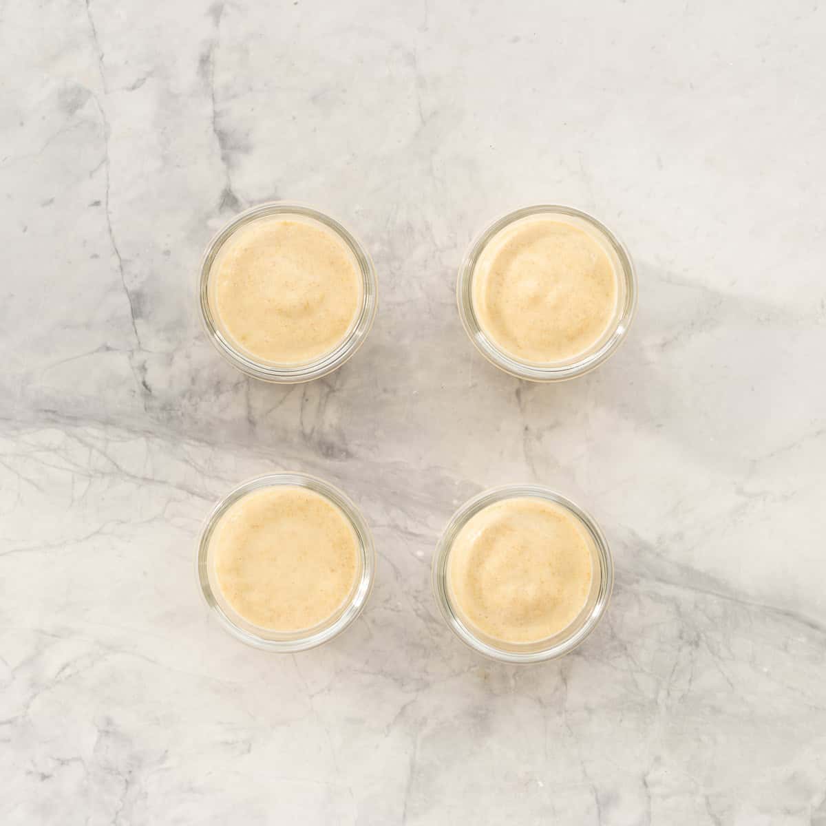 Four small glass jars filled with peach pudding on a bench top. 