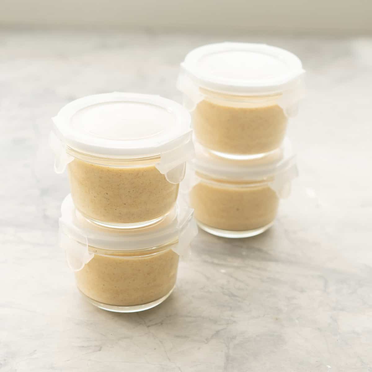 Four small glass jars filled with pudding with lids in place, stacked in two towers of two jars. 