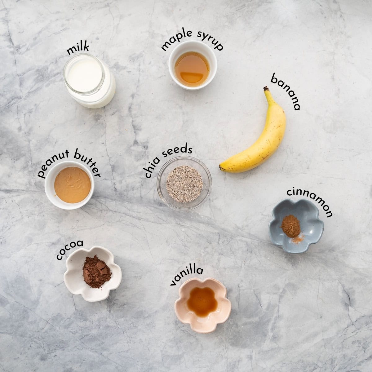Small bowls and jugs of ingredients: milk maple syrup banana, chia seeds, vanilla, cinnamon and peanut butter. 