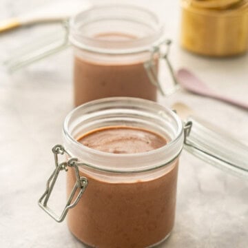 Two open glass jars of chocolate chia pudding on a bench with brass measuring cups in the background.