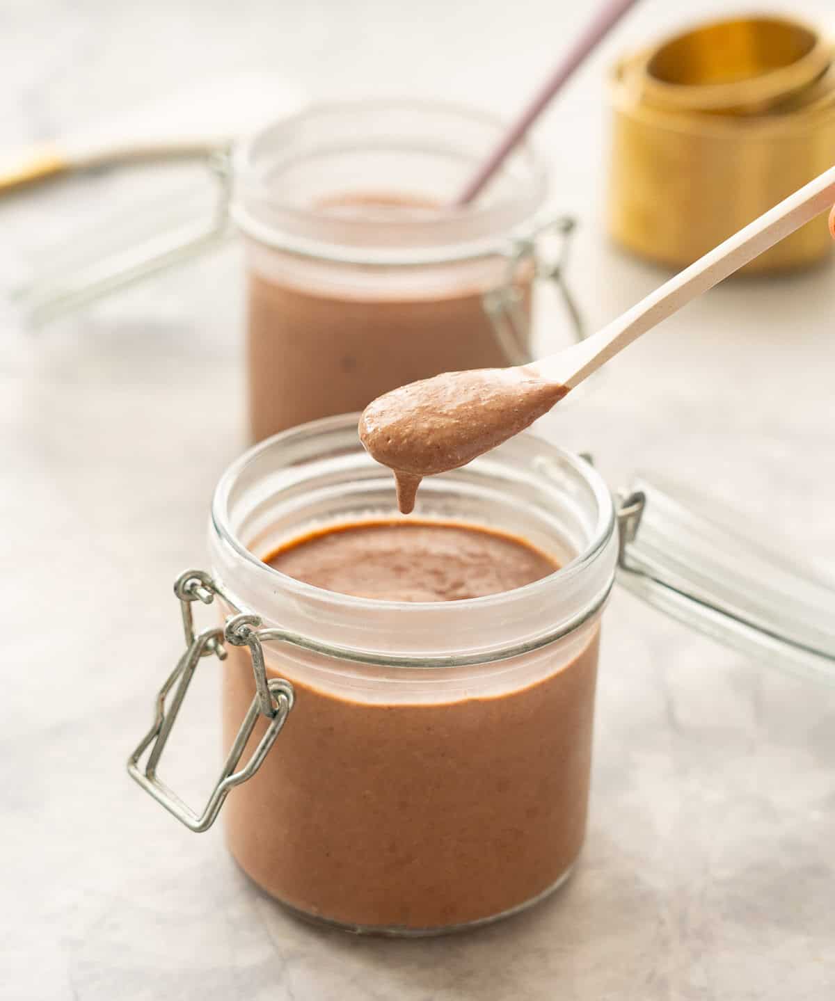 A spoonful of chocolate pudding being scoped from a small glass mason jar. 