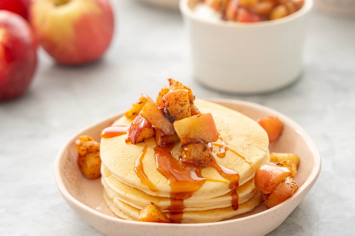 A stack of pancakes topped with cubes of cooked apples and a drizzle of golden syrup. 