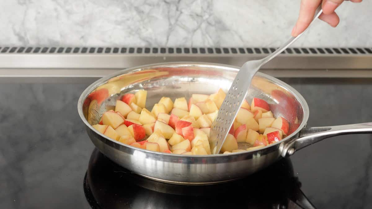 Cubes of apple with pink skins being cooked in butter on a stove top. 