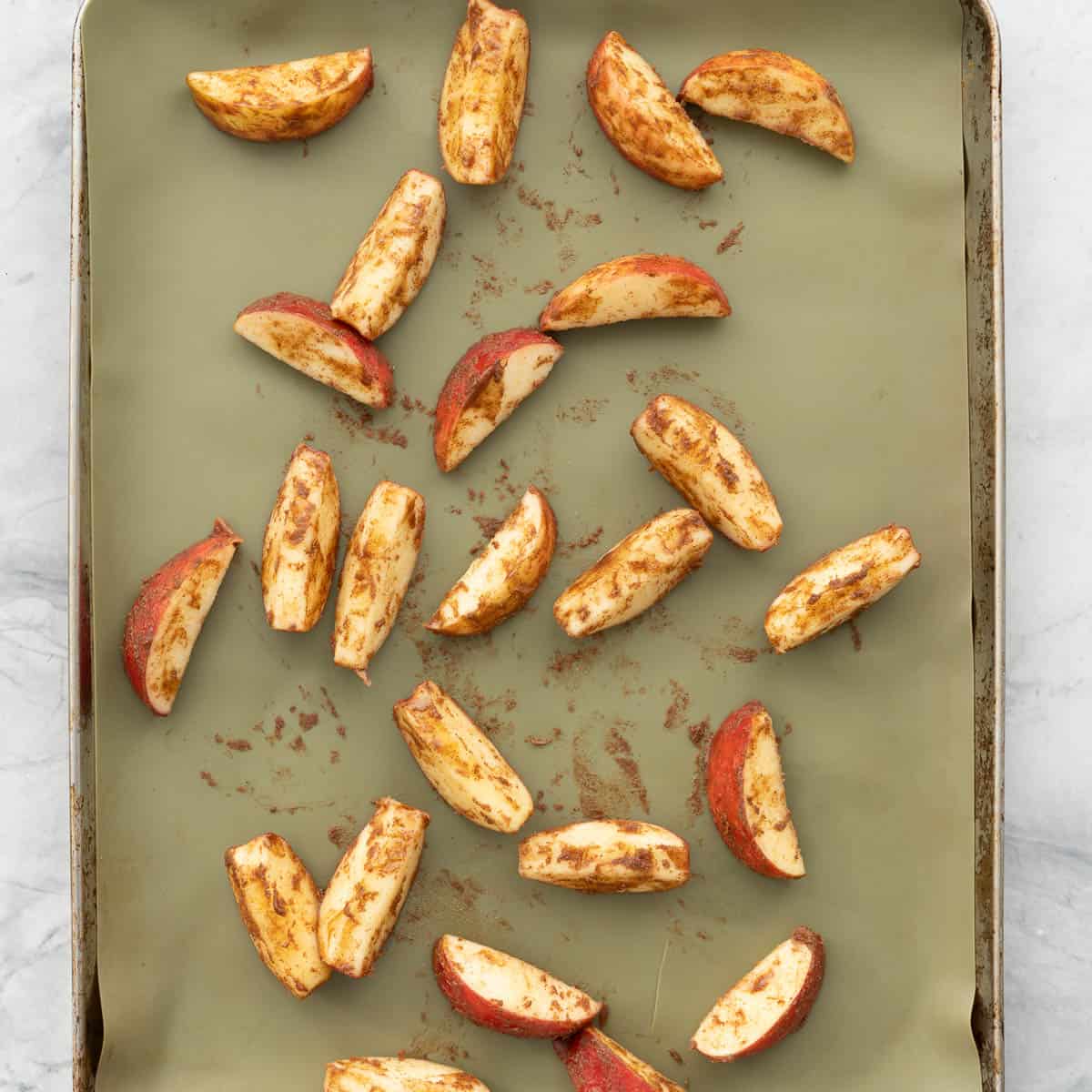 Cinnamon coated apple slices on a lined baking tray ready to go into the oven. 