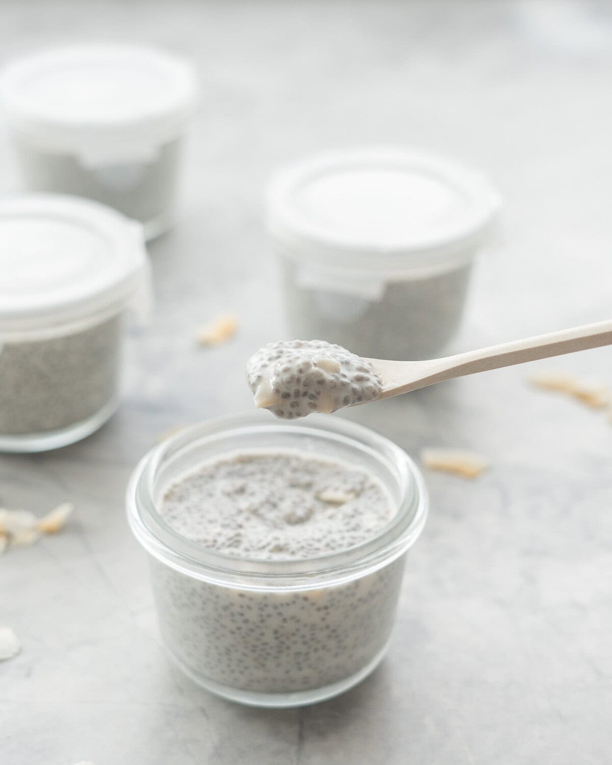 A spoonful of coconut and chia pudding above of small glass container filled with pudding.