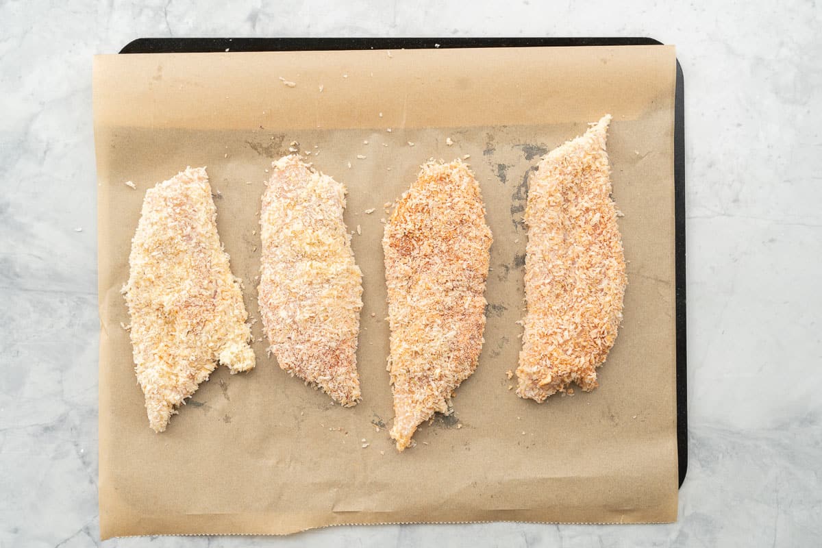 Crumbed chicken cutlets lying on a lined baking sheet ready to go into the oven. 