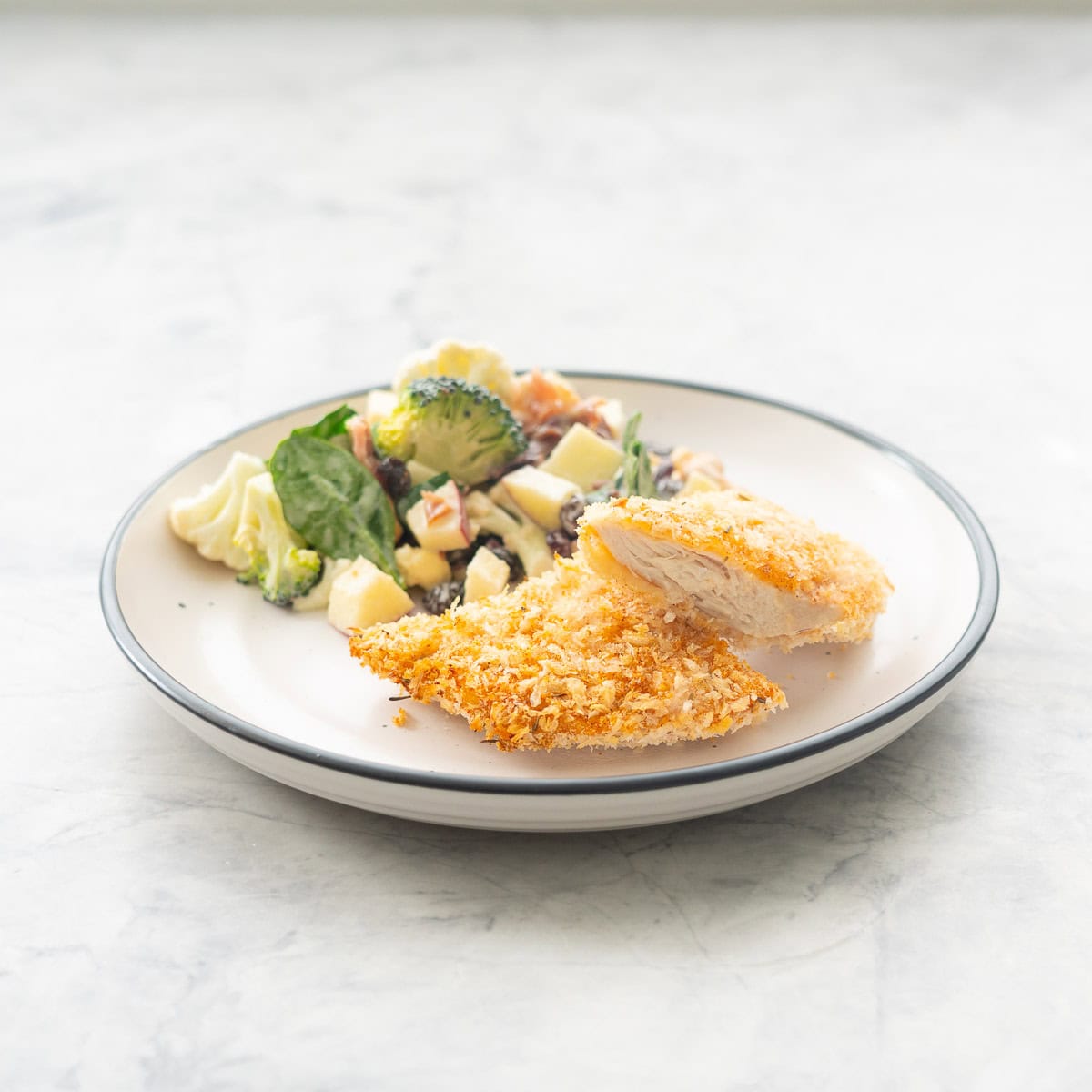 A white dinner plate with a crumbed chicken cutlet and broccoli salad. 