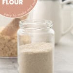 One jar of oat flour resting on the bench in front of a container of oats.n With text overlay: Homemade oat flour, tasty to make and nutritious.