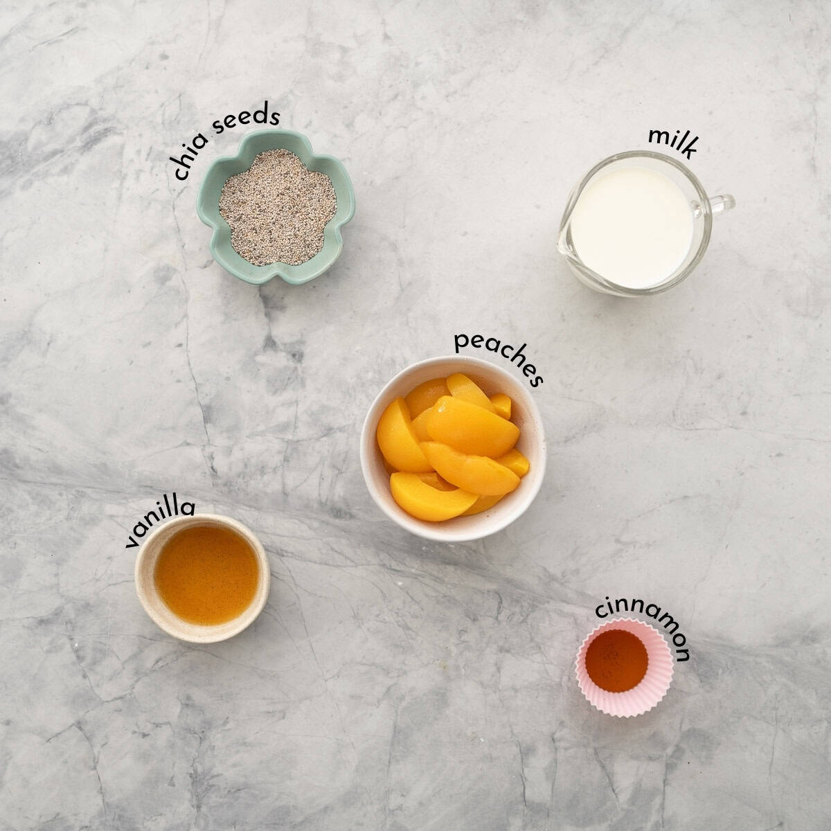 Bowls of peaches, chia seeds, vanilla, cinnamon and milk on a bench top, with text overlay ingredient labels.
