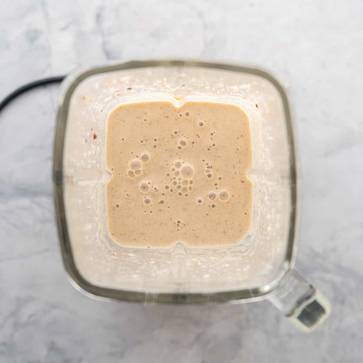 A glass blender filled with a light brown smoothie.