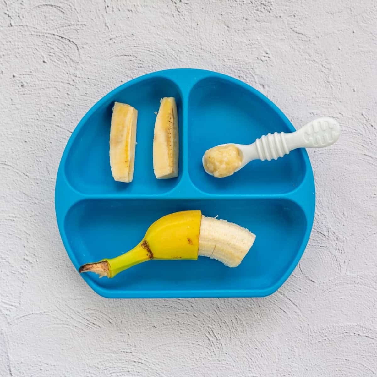 A blue divided plate with three ways to serve banana to babies. 