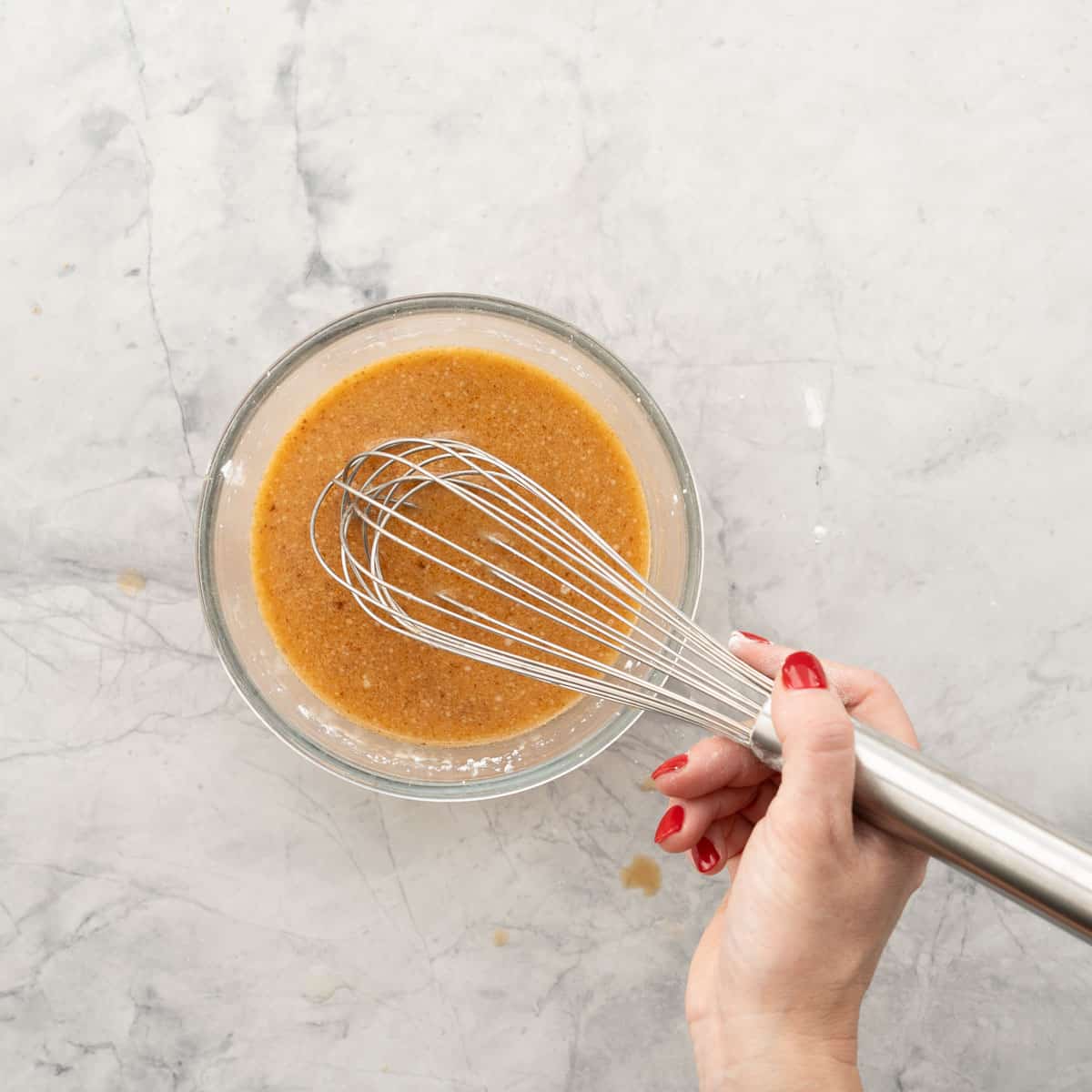 Marinade mixture being stirred with a whisk in glass bowl on bench top.