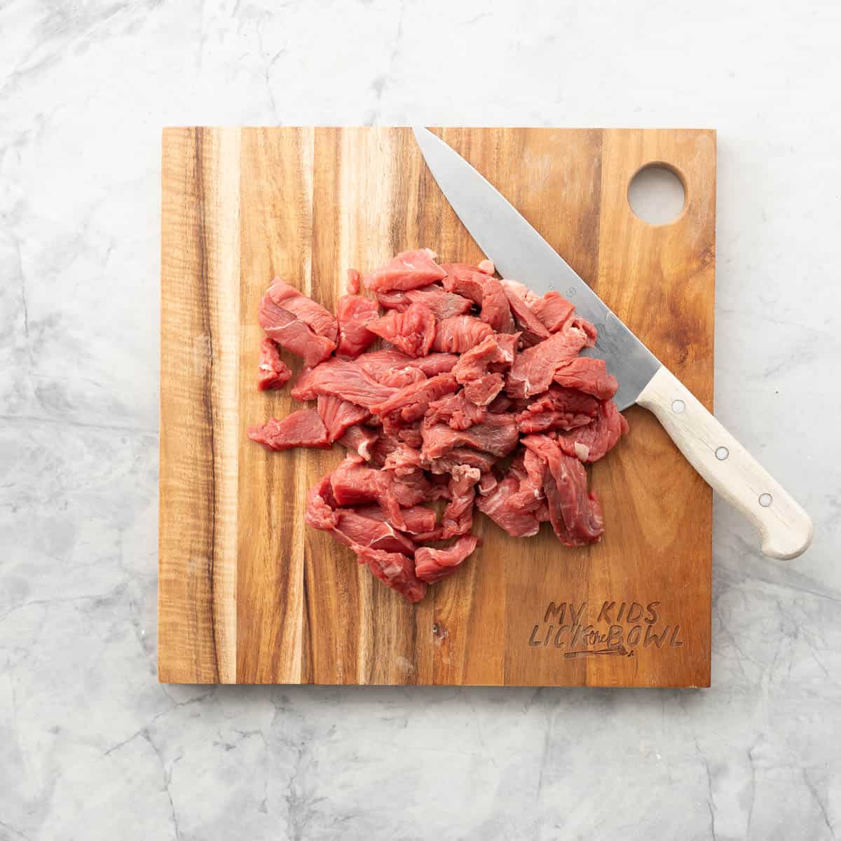 Uncooked sliced beef on chopping board with knife.