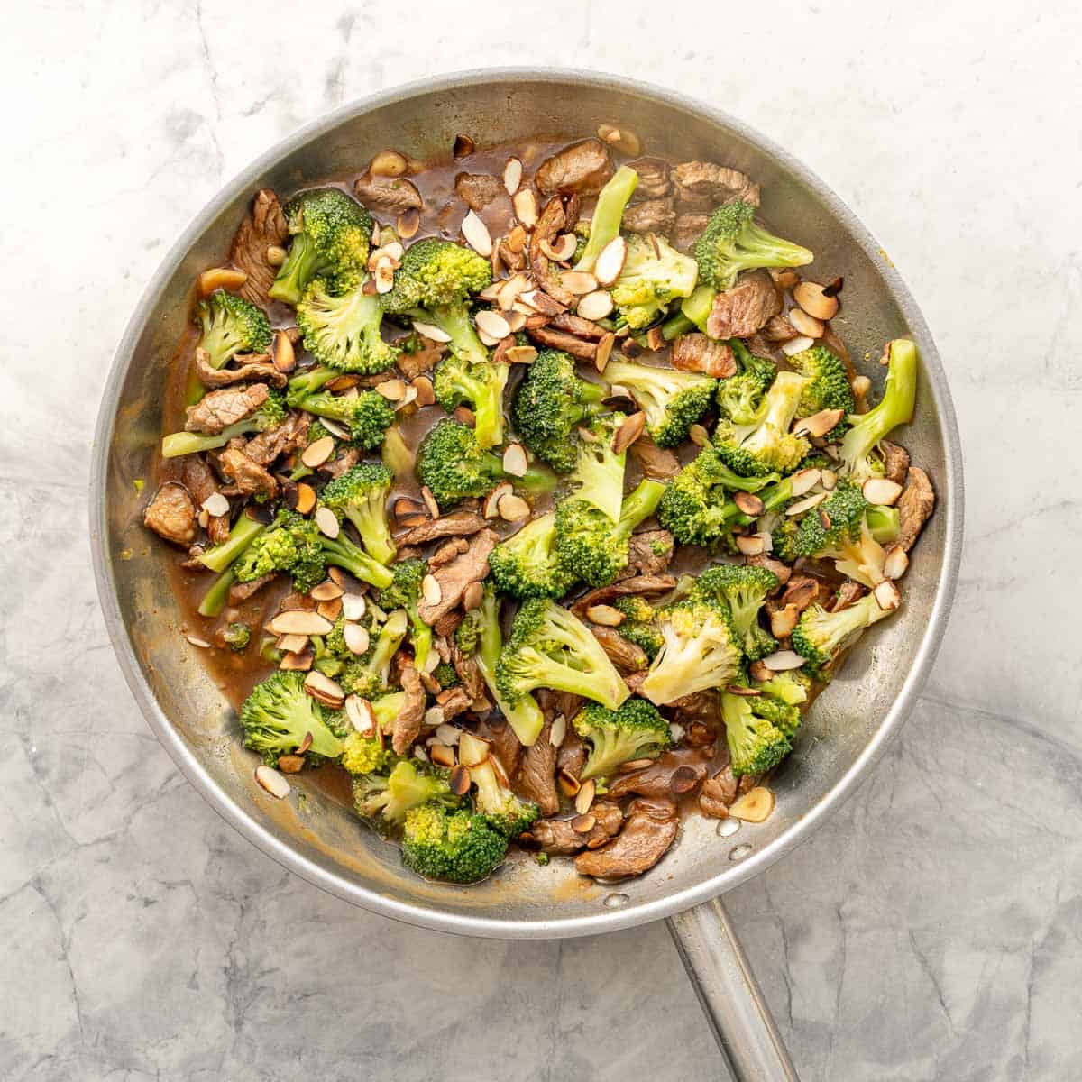 Beef and broccoli stir fry in pan with spoon ready to serve, chopped almonds garnished on top.