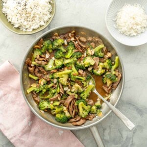 Beef and broccoli stir fry in pan with spoon ready to serve, chopped almonds garnished on top.